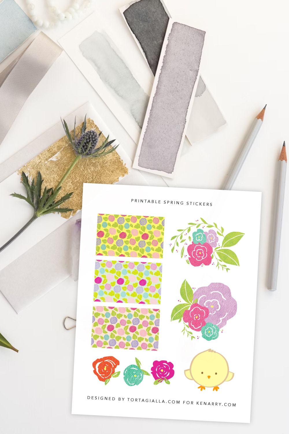 Preview of spring stickers printable page on top of a white desk with paint swatches on white papers, pencils and a lavender stem o the right. 