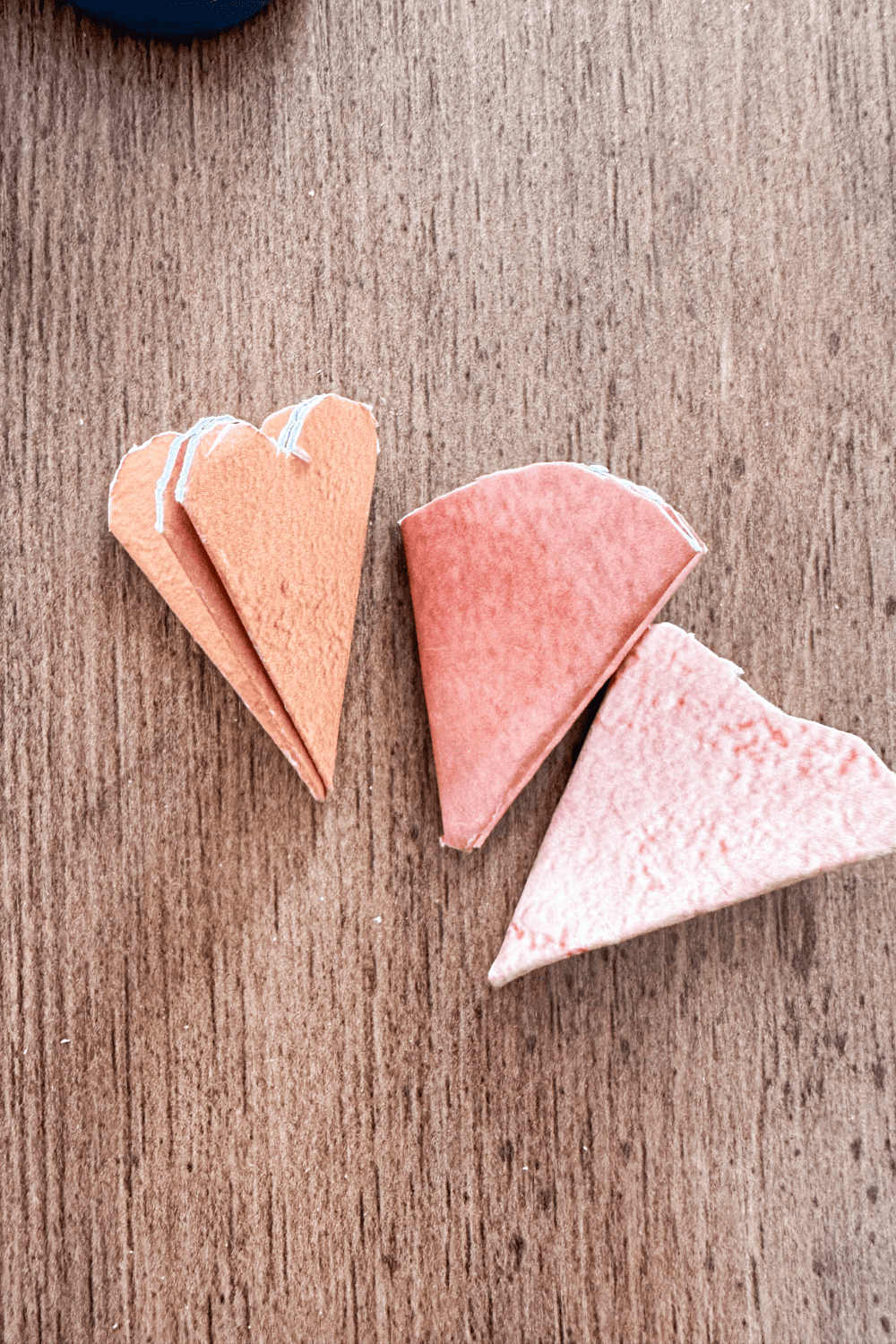 folded up paper. Left to right, orange with a heart cut, red with an arch cut, pink with a wave cut