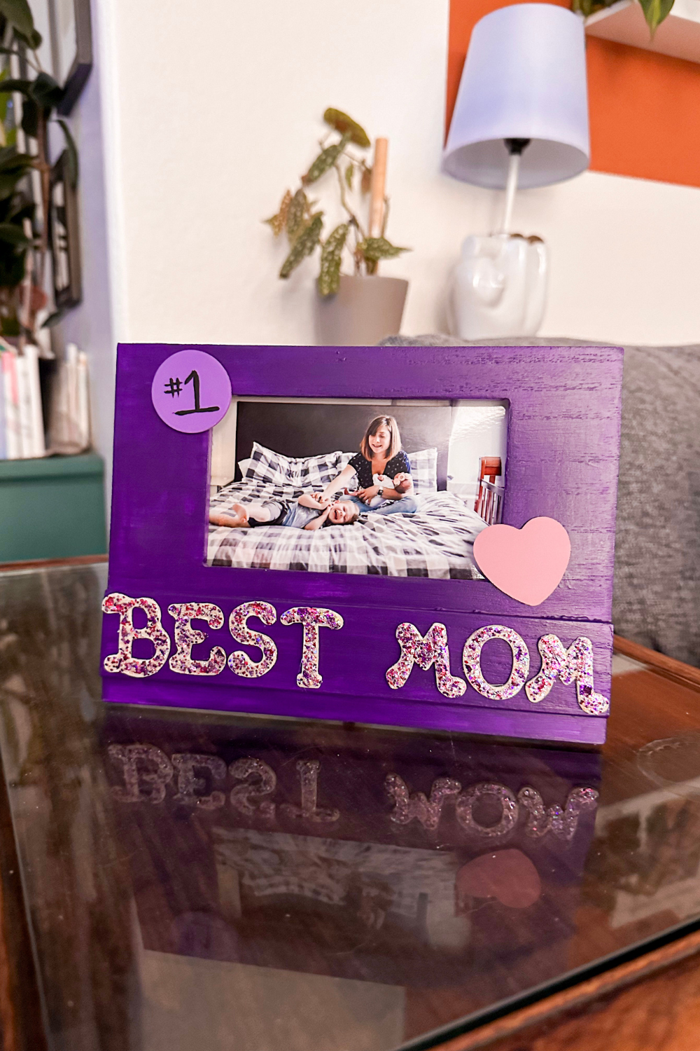 Purple picture frame that has best Mom in glitter letters. A picture is inside of a mother sitting with her two children.