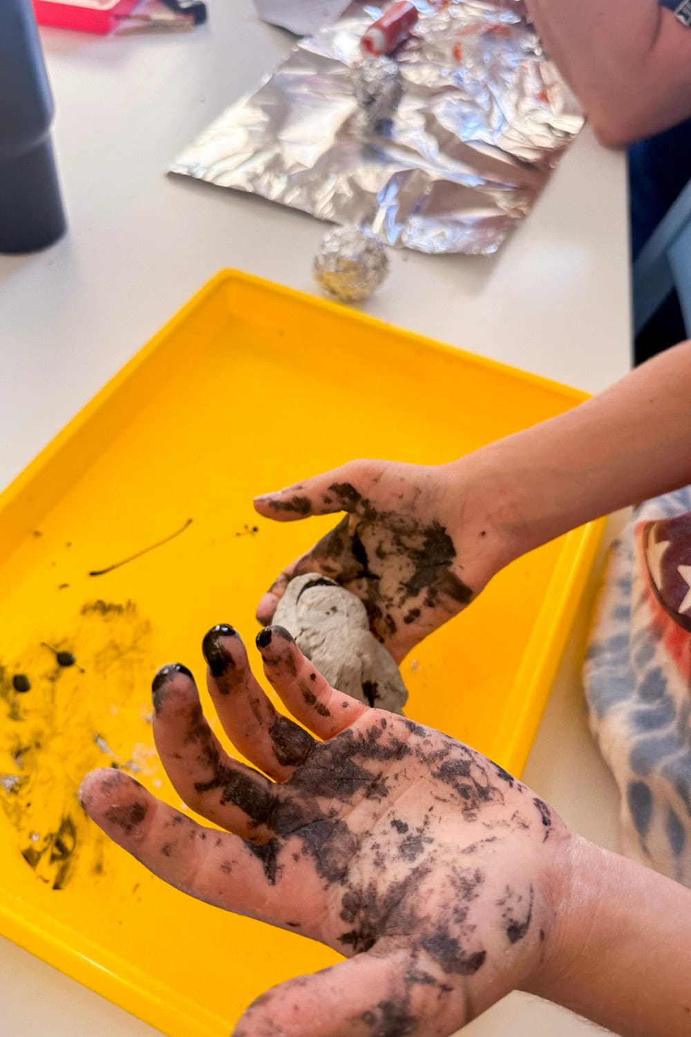 hands with black paint all over them and one of the hands holding clay in the background