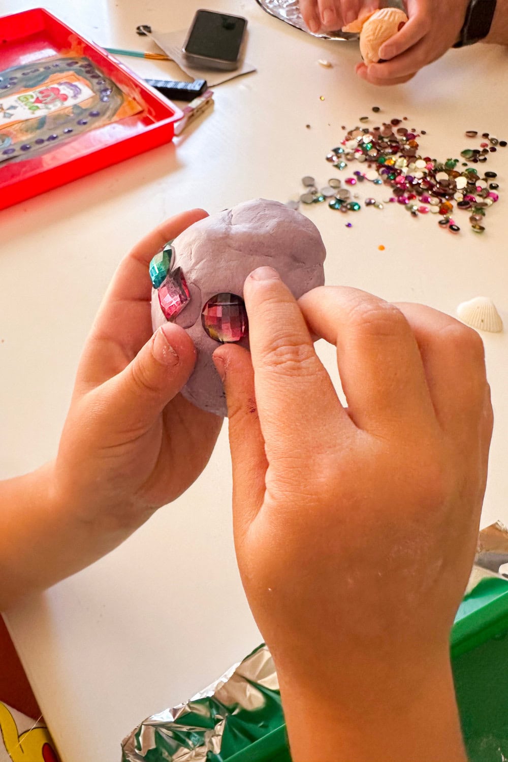 hands placing gems on a purple clay egg with gems in the background on the table